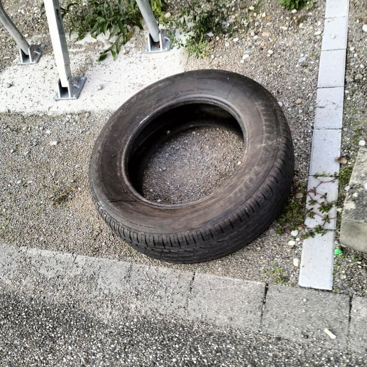 Un pneu usagé et emballage polystyrène abandonnés sur un parking privé 