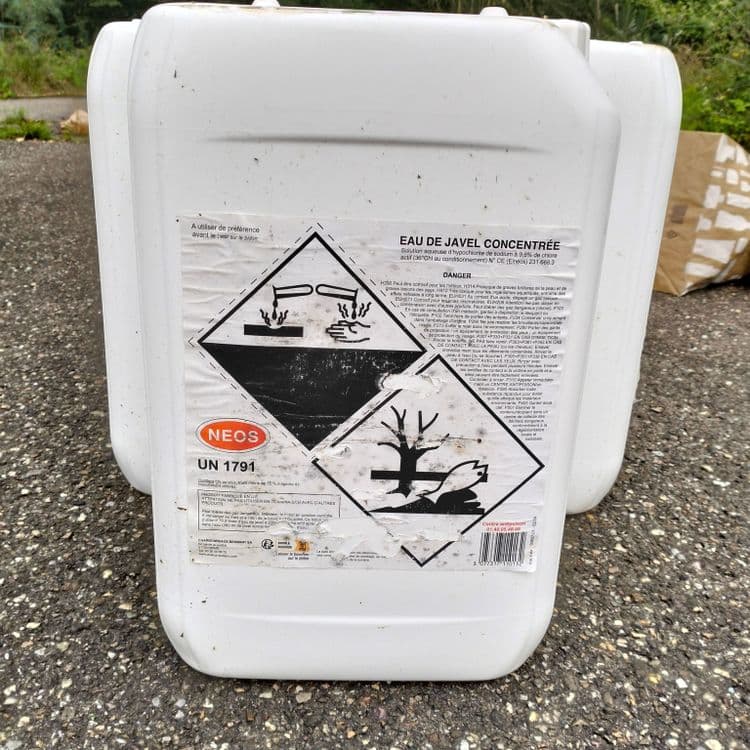 Bidons vides d'eau de javel concentrée et déchets divers abandonnés au bord d'un chemin en lisière de forêt 