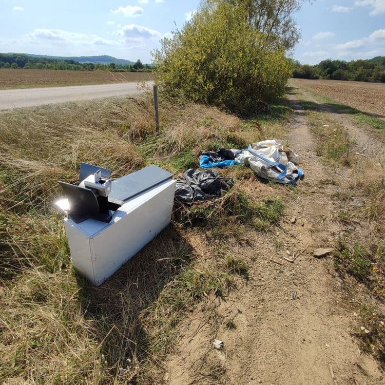 Voici l'analyse des déchets présents sur l'image :

*   Un appareil multifonction (imprimante/scanner) : Environ 20 kg, quantité : 1 unité.
*   Sacs poubelles noirs : Environ 5 kg par sac, quantité : 2 sacs.
*   Déchets divers (plastique bleu, sacs en toile) : Environ 3 kg, quantité : Indéterminée (plusieurs éléments).