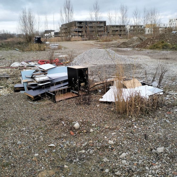 Mobilier, pièces automobiles, déchets divers sur un terrain vague à proximité de constructions neuves 