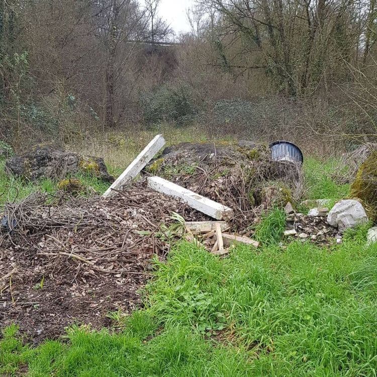 Voici une estimation des déchets présents sur le site :

*   **Gravats et débris de construction :** Il semble y avoir des morceaux de béton (environ 20 kg), des pierres et des restes de matériaux de construction (environ 15 kg).
*   **Végétaux :** Une quantité importante de branchages, feuilles mortes et autres déchets verts est visible (environ 30 kg).
*   **Bois :** Des éléments en bois, peut-être issus de débris de construction ou d'anciens meubles, sont présents (environ 10 kg).
*   **Métaux :** Un bidon métallique est visible (environ 5 kg). Il pourrait y avoir d'autres éléments métalliques enfouis dans les déchets.
