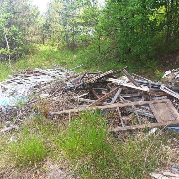 Depot sauvage de divers déchets, matériaux et objets hors d'usage (gravats, bois, vieil électroménager, pneus, etc). Plusieurs tas le long de la petite route.