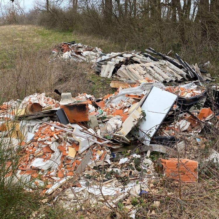 Déchets constatés sur la photo :

- **Tuiles et briques cassées :** Il semble y avoir une grande quantité de tuiles et de briques brisées, représentant probablement plusieurs centaines de kilogrammes, voire plus d'une tonne, en fonction de la profondeur du tas.  On estime la quantité à plus d'un mètre cube.

- **Débris de bois :**  Des morceaux de bois, certains semblent brûlés, sont visibles.  Le poids est difficile à estimer précisément, mais on peut imaginer une quantité entre 50 et 150 kg,  soit un volume d'environ 0.2 à 0.6 mètre cube.

- **Débris de plaques ondulées :**  Plusieurs plaques ondulées, apparemment en amiante-ciment (à vérifier impérativement), sont mélangées aux autres déchets. Leur poids est estimé entre 100 et 200 kg, soit un volume compris entre 0.5 et 1 mètre cube.  **ATTENTION : La présence éventuelle d'amiante nécessite une procédure de gestion spécifique et des équipements de protection.**

- **Déchets divers :**  On observe également des morceaux de plastiques, de métal, des débris de plâtre et d’autres matériaux de construction indéterminés. La masse de ces déchets est estimée entre 50 et 100 kg, avec un volume difficile à estimer avec précision.

**Estimation globale :** Le poids total des déchets est estimé entre 700 kg et 1500 kg, voire plus en fonction de la partie enfouie et non visible.  Un volume global estimé entre 2 et 3 mètres cubes.  Une intervention rapide est nécessaire compte tenu de la quantité importante de déchets et de la présence potentielle d'amiante.




