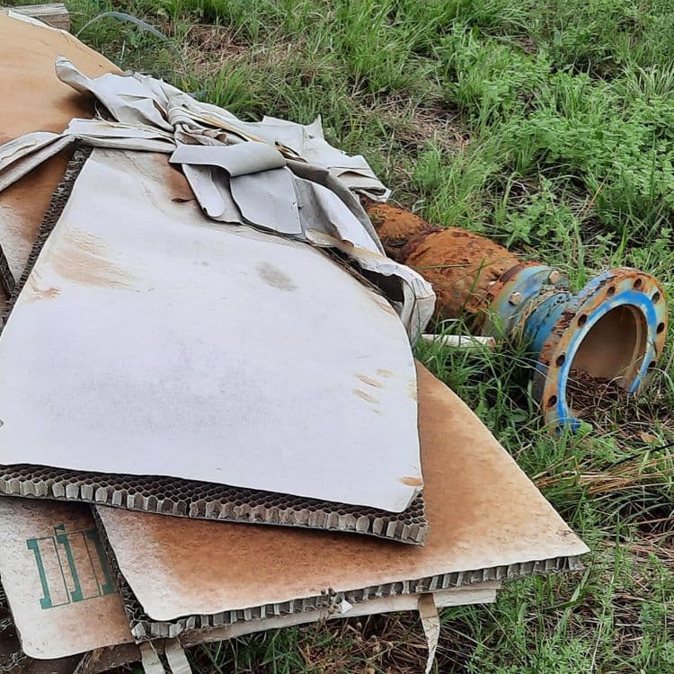 Voici une estimation des déchets présents sur le site :

*   **Carton alvéolaire:** On observe une quantité significative de carton alvéolaire, probablement issu d'emballages. Il y a au moins 3 plaques bien visibles, plus des fragments. Poids estimé : 5-10 kg.
*   **Tissus/Plastiques:** Des morceaux de tissus ou plastiques blancs sont présents, probablement des restes d'emballage ou de protection. Quantité : quelques fragments. Poids estimé : moins de 1 kg.
*   **Tuyauterie métallique:** Un tronçon de tuyauterie en métal rouillé est visible, avec une bride bleue.  Poids estimé : 10-20 kg.