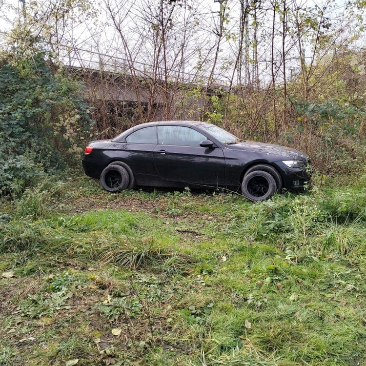 Véhicule semblant être abandonné au fond d'un parking sauvage, et deux pneus usagés abandonnés 