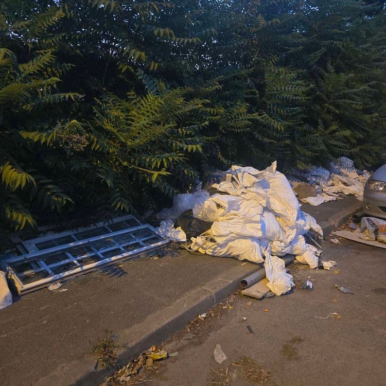 Voici le détail des déchets abandonnés sur le site :

*   **Sacs de gravats ou de déchets de chantier :** Une quinzaine de sacs de grande taille, principalement de couleur blanche, formant un monticule important. L'estimation du poids total est d'environ 400 kilogrammes.
*   **Cadres de fenêtre :** Deux cadres de fenêtre, probablement en bois ou PVC avec vitrage, sont posés au sol. Le poids estimé pour ces deux éléments est de 40 kilogrammes.
*   **Sacs poubelles noirs :** Environ quatre sacs poubelles noirs, contenant vraisemblablement des déchets ménagers ou divers. Le poids total est estimé à 30 kilogrammes.
*   **Tuyaux ou conduits :** Deux à trois sections de tuyaux, de couleur grise, sont visibles près du tas de sacs. Le poids estimé pour ces éléments est de 10 kilogrammes.
*   **Débris divers et petits détritus :** Une quantité éparse de petits déchets tels que des emballages, des morceaux de plastique et des débris végétaux mélangés. Le poids estimé pour l'ensemble est de 10 kilogrammes.
*   **Autres débris de construction :** Quelques planches ou morceaux de matériaux de construction épars. Le poids estimé est de 20 kilogrammes.