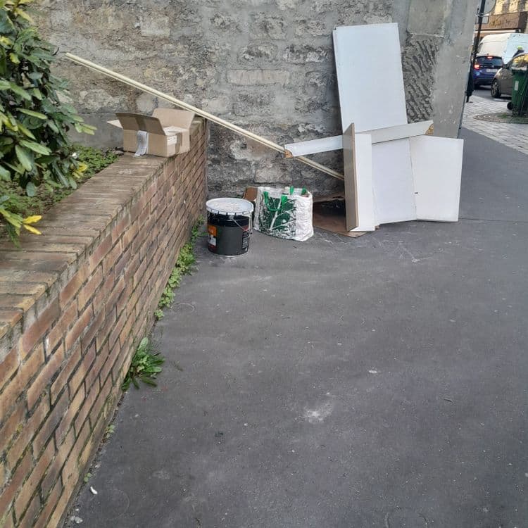 Il y a des planches en bois ,un seaux de peinture, un sac rempli de bouteille et du carton 