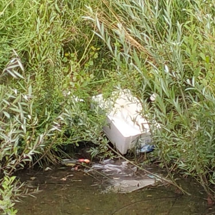 Pneus usagés, déchets divers, sacs poubelles dans une mare à côté d'un parking de zone commerciale 
