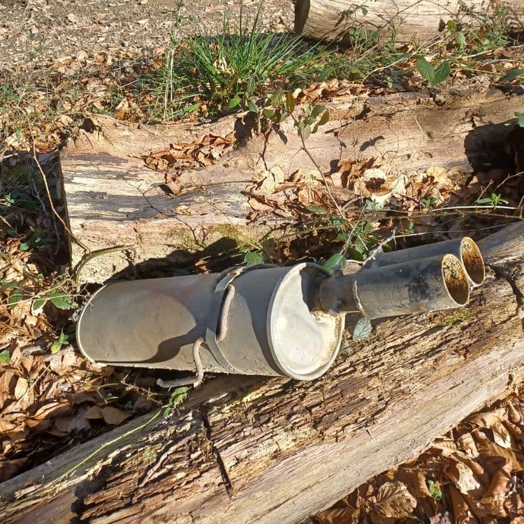 Echappement/silencieux de voiture posé au bord du chemin Henri 4 sur 2 troncs d arbres 