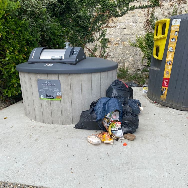 Voici une évaluation des déchets présents sur le site :

*   **Sacs poubelles noirs:** On observe environ 5 sacs poubelles noirs. Estimons un poids moyen de 5 kg par sac, ce qui donne un total de 25 kg. Contenu indéterminé (ordures ménagères probables).
*   **Sac poubelle bleu (semi-transparent):** Un sac est visible avec un contenu apparent. On y distingue des emballages alimentaires, des restes de nourriture (dont une peau de banane), et divers autres déchets ménagers. Estimation du poids : 3 kg.
*   **Déchets éparpillés:** On note la présence de divers déchets épars autour des sacs :
    *   Emballages carton et plastique : estimons 0.5 kg au total pour ces déchets.
    *   Restes de nourriture (épluchures, etc.): environ 0.2 kg.
    *   Divers petits débris (papier, etc.): 0.1 kg.
*   **Autres déchets:**
    *   Un pot de peinture vide : 0,5 kg
    *   Un Camel : 0,1 kg

En résumé, le site présente un mélange d'ordures ménagères en sacs et de déchets divers éparpillés, totalisant environ 29,4 kg.

