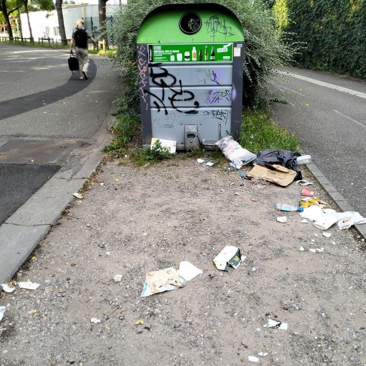 Sac poubelle et déchets ménagers à côté d'un container à verre et proche piste cyclable 