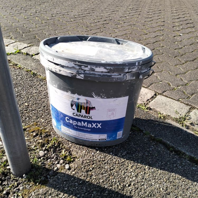 Sceau de peinture ou colle abandonné sur un trottoir 