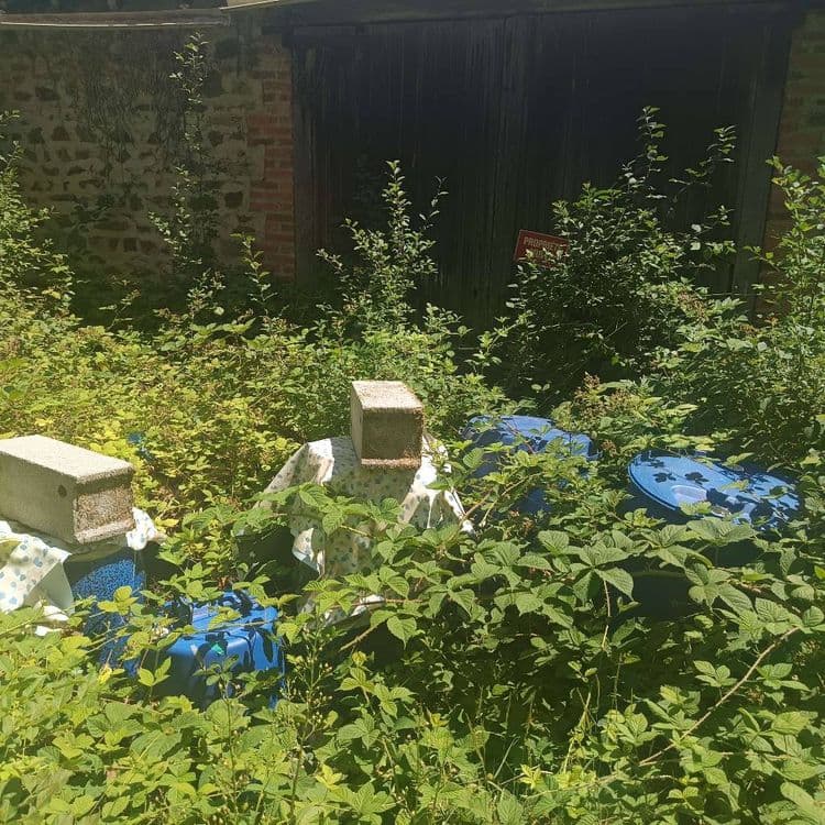 Objets métalliques et fûts de déchets industriels ayant débordé lors des pluies (se remplissent d'eau, les huiles et hydrocarbures débordent sur les sols) à 15 m au dessus d'une source