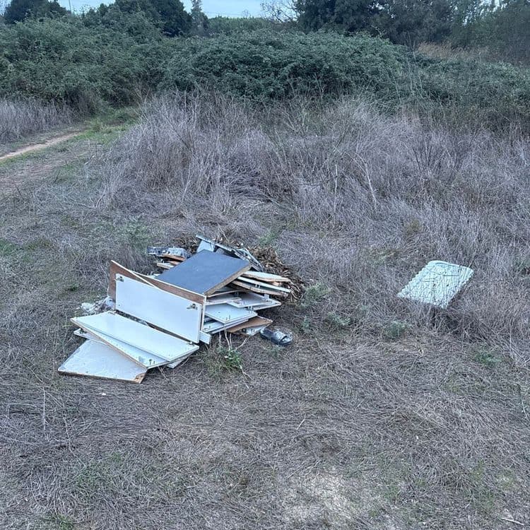 Voici le détail des déchets abandonnés sur le site :

*   **Panneaux de mobilier en bois aggloméré ou mélaminé** : Il s'agit principalement de portes de placards, d'étagères et de côtés de meubles démontés. On dénombre environ 12 à 15 pièces de différentes tailles. Le poids total estimé pour ce type de déchet est de 50 à 60 kilogrammes.
*   **Petits éléments de mobilier et quincaillerie** : Quelques morceaux de bois plus petits et des éléments de fixation (charnières, vis) sont mélangés aux panneaux. Leur quantité est faible, et leur poids est inclus dans l'estimation des panneaux, représentant environ 2 à 3 kilogrammes supplémentaires.
*   **Objet en plastique blanc** : Une pièce unique, de forme rectangulaire, qui pourrait être un abattant de toilettes ou un couvercle de réservoir. Son poids est estimé entre 1 et 2 kilogrammes.
*   **Objet divers** : Un unique objet sombre, ressemblant à une chaussure ou une sandale. Son poids est estimé à moins de 1 kilogramme, environ 0.5 kilogramme.