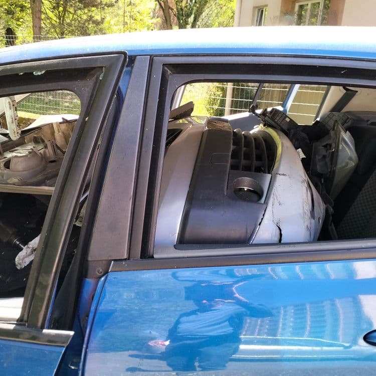 Véhicule abandonné sur un parking public avec des pièces détachées 