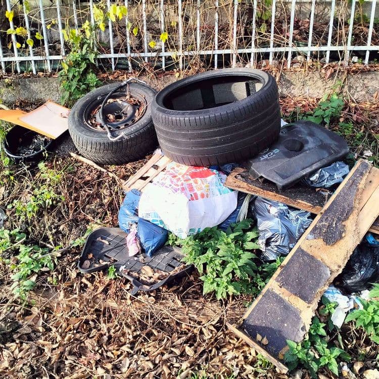 Pneus usagés et huile de vidange et déchets divers abandonnés sur un parking de jardins ouvriers 