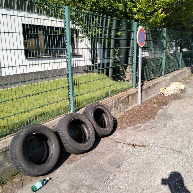 Pneus usagés et emballage divers à côté d'une aire de lavage sur parking de supermarché 
