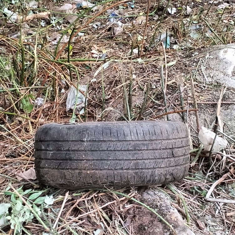 Détritus et déchets divers, pneu usagé abandonnés sur un terrain en bordure d'un parking de supermarché 