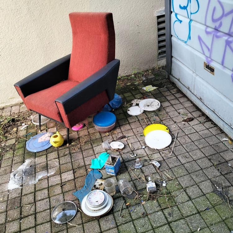 Vieux fauteuil et vaisselle cachés derrière un container à verre 