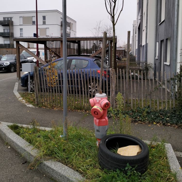 Pneu usagé et déchets divers abandonnés à côté d'une borne incendie en quartier résidentiel 
