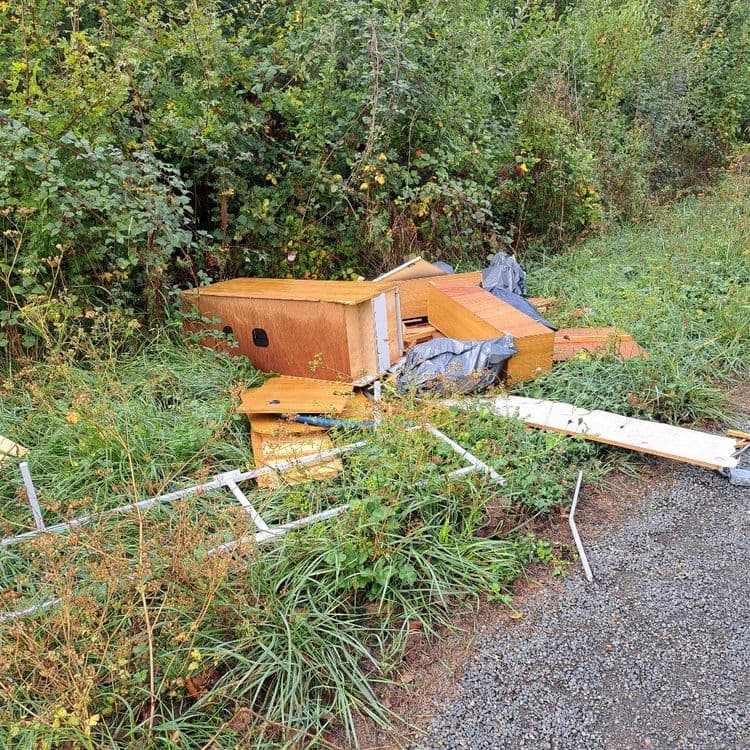 Voici les types de déchets abandonnés sur le site, avec une estimation de leur quantité et de leur poids :

*   **Déchets d'ameublement en bois:** Il s'agit principalement de panneaux d'aggloméré et de contreplaqué provenant de meubles démontés (corps de placards, étagères, façades de tiroirs).
    *   Quantité estimée: L'équivalent de 3 à 4 meubles de taille moyenne.
    *   Poids estimé: Environ 90 kg.

*   **Sacs poubelles noirs:** Ces sacs contiennent probablement des déchets ménagers ou des petits encombrants.
    *   Quantité estimée: 2 à 3 sacs.
    *   Poids estimé: Environ 15 kg.

*   **Structure métallique:** Des éléments tubulaires en métal, possiblement issus d'un cadre de lit, d'une étagère ou d'un support.
    *   Quantité estimée: Plusieurs sections formant une structure partielle.
    *   Poids estimé: Environ 15 kg.

*   **Déchets divers (câble électrique, tuyau flexible):** Un câble électrique et un morceau de tuyau en plastique.
    *   Quantité estimée: 1 câble, 1 tuyau.
    *   Poids estimé: Moins de 1 kg.