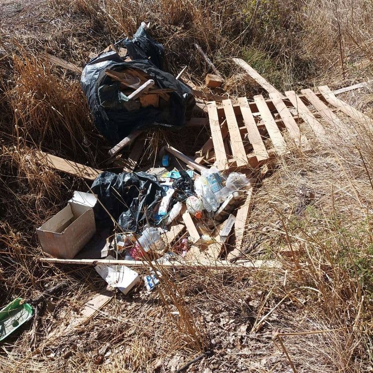 Voici le relevé des déchets abandonnés sur le site :

*   **Bois :** Il s'agit principalement de palettes en bois cassées et de planches diverses. On estime la quantité à l'équivalent de 2 à 3 palettes complètes, plus des chutes de bois. Le poids total est estimé à environ 70 kilogrammes.
*   **Sacs poubelles noirs :** Deux grands sacs sont présents, contenant un mélange de déchets ménagers et de petits débris. Le poids estimé pour ces deux sacs est de 25 kilogrammes.
*   **Bouteilles et emballages plastiques :** Une vingtaine à une trentaine de bouteilles d'eau et de boissons, ainsi que divers emballages en plastique, sont dispersés. Le poids total est d'environ 1,5 kilogramme.
*   **Cartons et papiers :** Un carton de grande taille ouvert et plusieurs petits morceaux de carton et de papier sont visibles. Le poids estimé est de 1 kilogramme.
*   **Déchets divers :** Cela inclut des emballages alimentaires, des petits objets non identifiables précisément et d'autres débris légers. La quantité est difficile à chiffrer précisément, mais le poids est estimé à 5 kilogrammes.
*   **Objet plastique vert :** Un bac ou une pelle en plastique de couleur verte est présent. Le poids est estimé à 0,5 kilogramme.