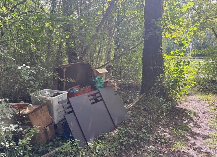 Les déchets abandonnés sur le site comprennent :

*   **Cartons d'emballage :** Une quantité estimée à 5 à 7 unités de tailles variées, pour un poids total d'environ 7 à 14 kilogrammes.
*   **Panneaux de bois ou aggloméré :** Il y a 3 grands panneaux sombres, mesurant approximativement 1 mètre par 0,8 mètre chacun, ainsi que des fragments de mobilier en bois. Le poids total est estimé entre 35 et 55 kilogrammes.
*   **Caisses en plastique :** Une caisse blanche est clairement visible, avec la possibilité de 1 à 2 autres moins distinctes. Le poids total est estimé entre 2 et 4 kilogrammes.
*   **Sac plastique :** Un sac de couleur verte est présent. Son poids est estimé entre 2 et 5 kilogrammes, selon son contenu.
*   **Déchets divers :** Quelques petits objets et fragments non identifiés précisément sont également présents, pour un poids estimé entre 3 et 5 kilogrammes.