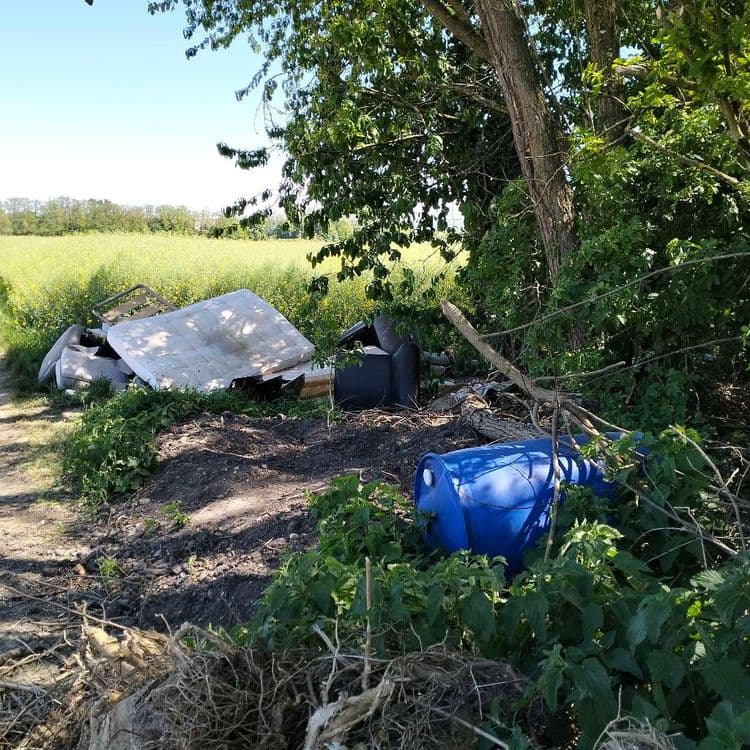 Bidons, mobilier et déchets divers abandonnés au bord d'un chemin au milieu des champs 