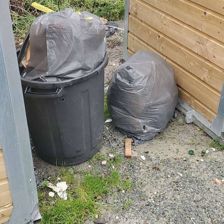 L'image révèle la présence de plusieurs types de déchets. On observe un sac poubelle noir plein, estimé à environ 10 kg. Un autre sac poubelle noir, également plein, est visible dans une poubelle noire. Le poids de ce sac est estimé à 12kg. On remarque également la présence de petits débris éparpillés au sol, tels que des morceaux de plastique blanc et un petit morceau de bois, dont le poids total est estimé à moins de 0.5 kg. Il y a aussi des opercules de bouteilles en plastique, au nombre de 2, pesant quelques grammes.
