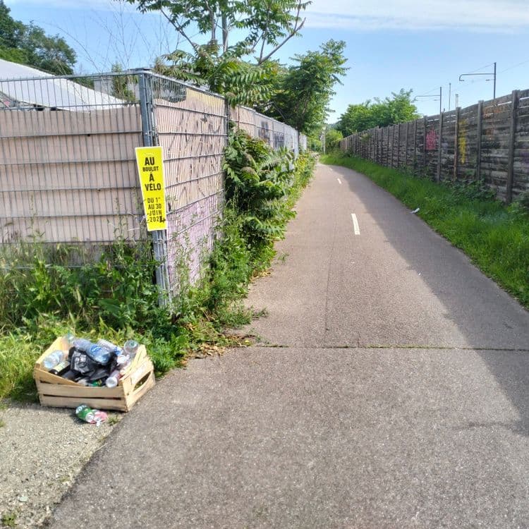 Cageot rempli de déchets divers au bord de la piste cyclable 