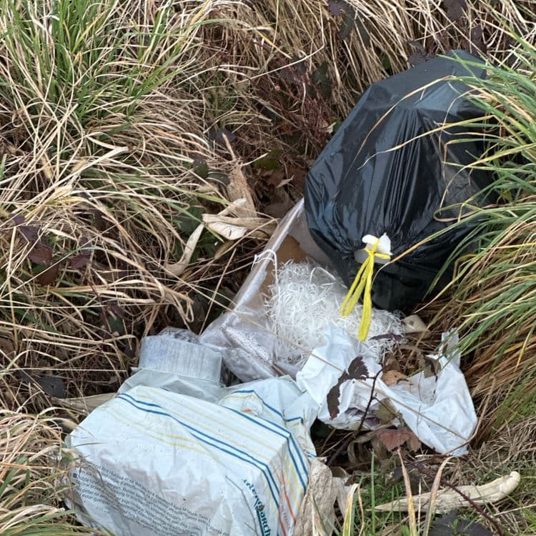 Liste des déchets abandonnés :

* **Sac poubelle noir :** Un sac poubelle noir d’environ 5 kg contenant des déchets non visibles. La taille du sac suggère une quantité importante de déchets.

* **Emballage en plastique transparent :** Un emballage en plastique transparent, probablement d’un colis, contenant des copeaux de papier blanc. Le poids estimé est de 0,5 kg, en incluant le contenu.

* **Emballage en plastique avec rayures :** Un emballage en plastique avec des rayures bleues et jaunes. Il pourrait s'agir d’un emballage alimentaire ou de livraison. Le poids estimé est de 0,3 kg.

* **Autres papiers/déchets :** Plusieurs petits morceaux de papier et d’autres déchets non identifiables, éparpillés autour des emballages plus importants. Le poids total estimé de ces déchets est de 0,2 kg.

Estimation du poids total des déchets : Environ 6 kg.  L’estimation est approximative et dépend de la densité des déchets dans le sac noir.

