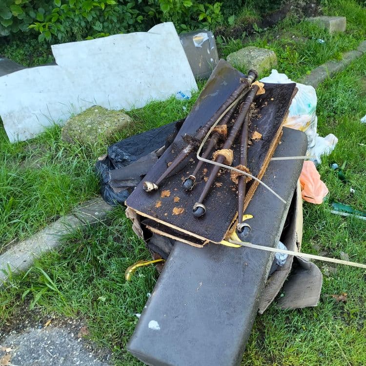 Déchets divers et reste de mobilier au fond d'un petit parking public 
