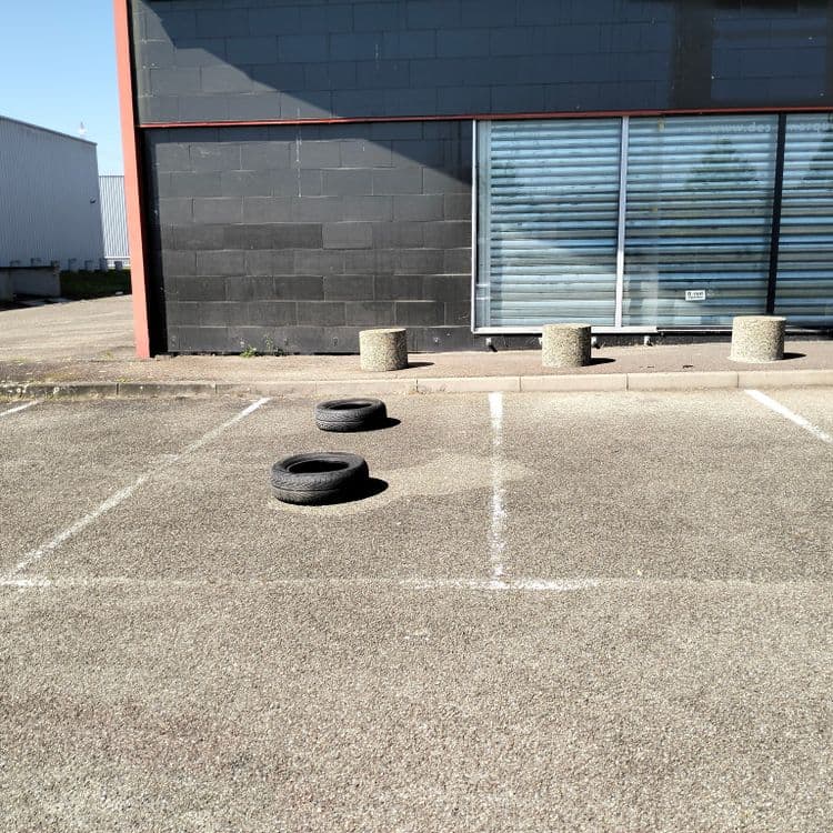 Deux pneus usagés abandonnés sur un parking de zone commerciale 