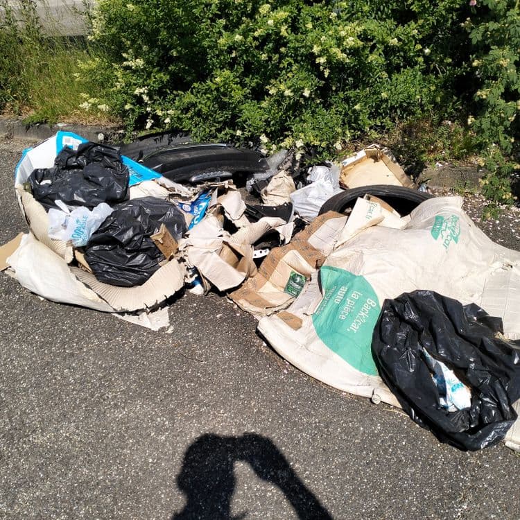 Pièces automobiles, pneus usagés et déchets divers abandonnés sur un parking de zone commerciale 