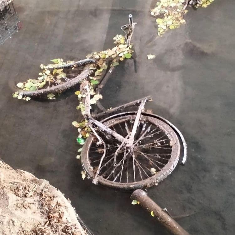 Caddies de supermarché, vélo, pneus usagés, cartouches de protoxyde d'azote dans une rivière, sous un pont routier 