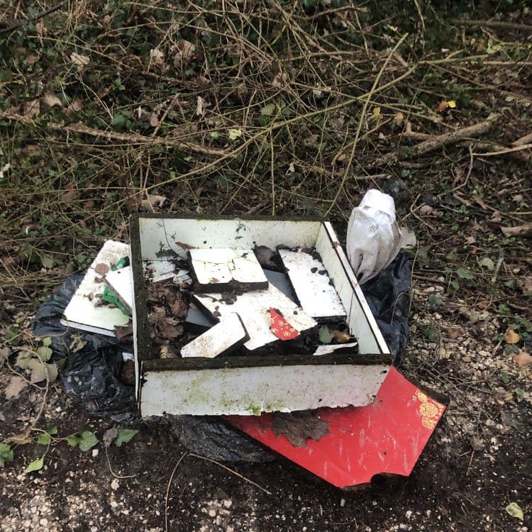 Déchets observés :

- **Bois et débris de lambris :** Il semble y avoir une caisse en bois ou un cadre de lambris blanc cassé, brisé en plusieurs morceaux.  Le poids estimé est d'environ 5 kg, la quantité étant estimée à 1 caisse/cadre.  Des débris de bois supplémentaires sont présents dans et autour de la caisse. Le poids supplémentaire de ces débris est estimé à 2 kg.

- **Plastique :** Un sac poubelle noir contient certains déchets. Le poids estimé du sac et son contenu est de 1 kg.  Une pièce blanche, qui pourrait être un sac plastique ou un autre emballage, est visible près du sac poubelle. On estime son poids à 0,5 kg.

- **Déchets divers :**  Des morceaux de ce qui semble être du carton ou du papier (rouge et autres) sont présents, ainsi que de petits débris indéterminés. Leur poids total est estimé à 1 kg.

En résumé, les déchets visibles sur la photo pèsent environ 9,5 kg au total et comprennent une caisse/cadre en bois, un sac poubelle contenant des déchets variés, du plastique et des déchets en papier/carton.
