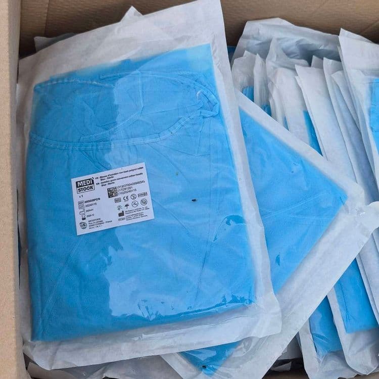 Dépôt sauvage comprenant : Un grand carton rempli de blouses médicales d'isolation bleues et stériles. Un barbecue noir en métal. Un carton déchiré vide.