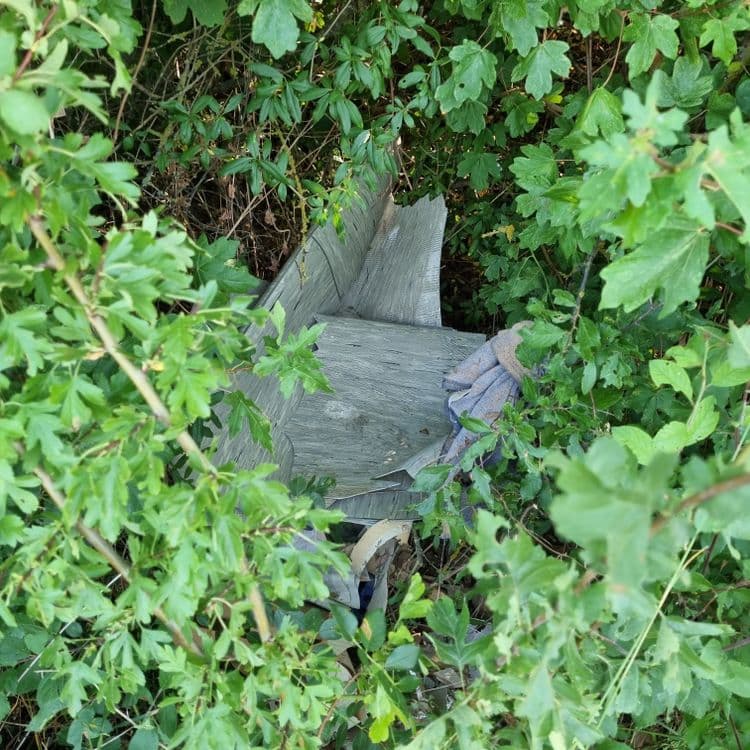 Es wurde illegal Bodenbelagreste aus PVC, Linoleum oder evtl. sogar Asbest in der Hecke entsorgt.