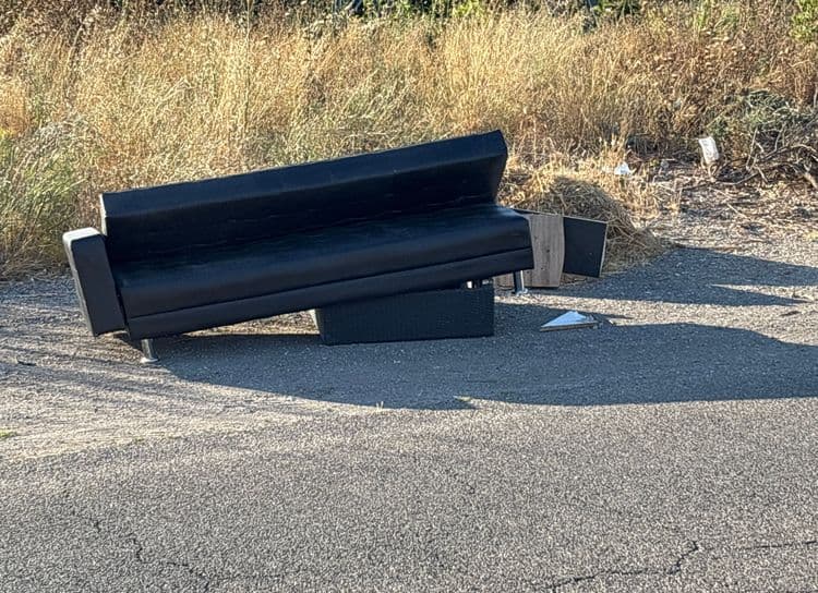 Voici l'analyse des déchets présents sur l'image :

Un canapé en simili cuir noir est visible, estimé à environ 30 kg. Une petite table d'appoint en résine tressée de couleur foncée est également présente, son poids est estimé à 5 kg. Des débris de bois (panneaux) sont éparpillés autour, représentant un poids approximatif de 3 kg. Enfin, on observe quelques déchets plastiques et papiers épars aux alentours, représentant environ 0.5 kg. 
