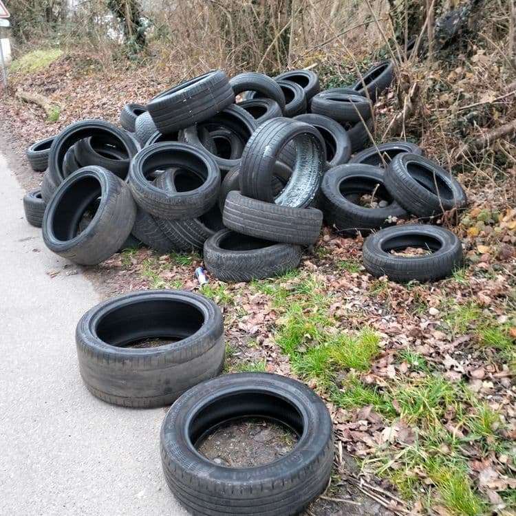 Plusieurs dizaines de pneus usagés abandonnés au bord de la route à proximité d'un terrain des gens du voyage 