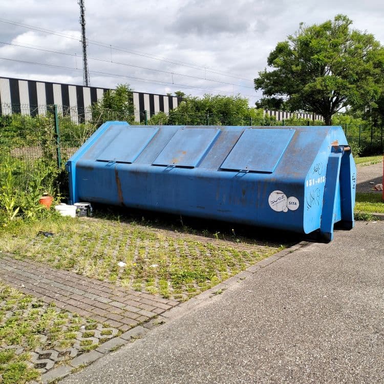 Pots de peinture à côté d'un container sur parking de zone commerciale 