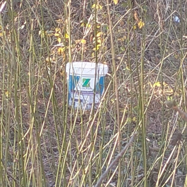 Pots de peinture abandonnés sur un talus, entre un parking public et l'autoroute, au bord d'un ruisseau 