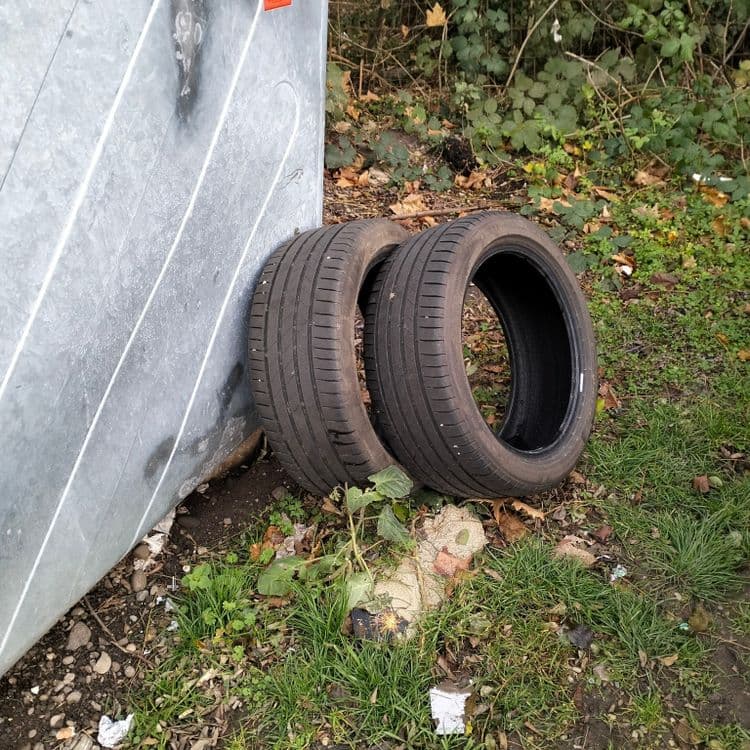 Deux pneus usagés abandonnés à côté d'une benne sur un parking public 