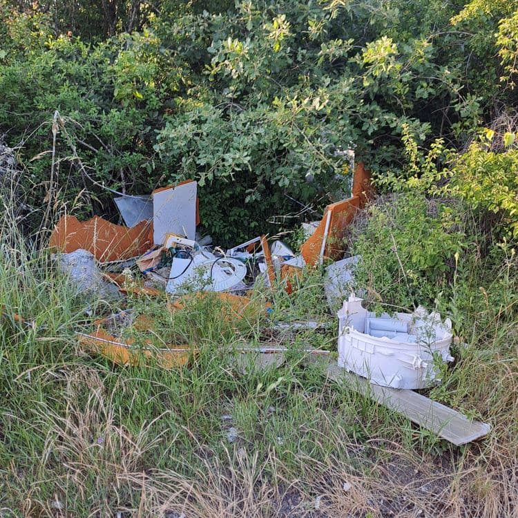 Voici une estimation des déchets présents sur l'image :

*   **Mobilier (fragments):** Divers morceaux de mobilier, possiblement d'une caravane ou d'un meuble de rangement (éléments de structure, panneaux, etc.). Estimation du poids total : 15 kg. Quantité : Fragments épars.

*   **Plastique rigide (éléments électroménagers):** Pièces de plastique blanc provenant d'un appareil électroménager (probablement une machine à laver ou un sèche-linge). Estimation du poids total : 5 kg. Quantité : 1.

*   **Isolant (orange) :** Matériau isolant orange, potentiellement de la mousse ou un matériau similaire utilisé dans la construction ou l'ameublement. Estimation du poids total : 2 kg. Quantité : Fragments épars.

*   **Métaux divers :** Petits éléments métalliques non identifiés. Estimation du poids total : 1 kg. Quantité : Petits fragments.

*   **Déchets divers indéterminés :** Divers petits débris et fragments non identifiables avec précision. Estimation du poids total : 1 kg. Quantité : Non quantifiable.
