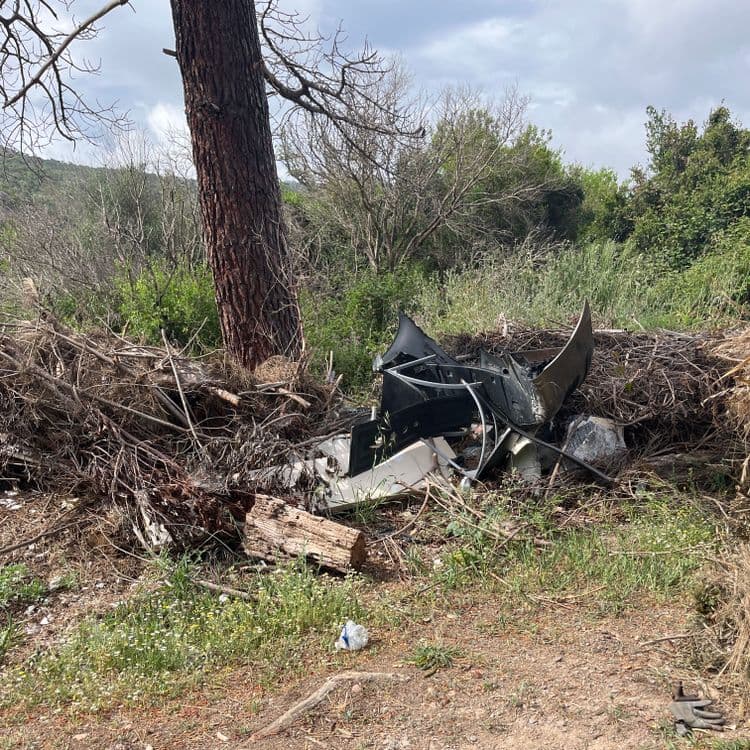 Voici une estimation des déchets présents sur la photo :

*   **Débris automobiles :** Divers fragments de carrosserie, plastiques, et potentiellement des éléments mécaniques. Poids estimé : 10 - 20 kg, Quantité : importante (plusieurs pièces).

*   **Déchets verts:** Branches, feuilles mortes, brindilles et autres résidus végétaux. Poids estimé : 5 - 10 kg. Quantité : importante.

*   **Bois:** morceau de bois. Poids estimé : 1 - 2 kg. Quantité : petit.

*   **Déchets plastiques :** Un sac plastique visible au premier plan. Poids estimé : moins de 0.1 kg. Quantité : un seul sac.