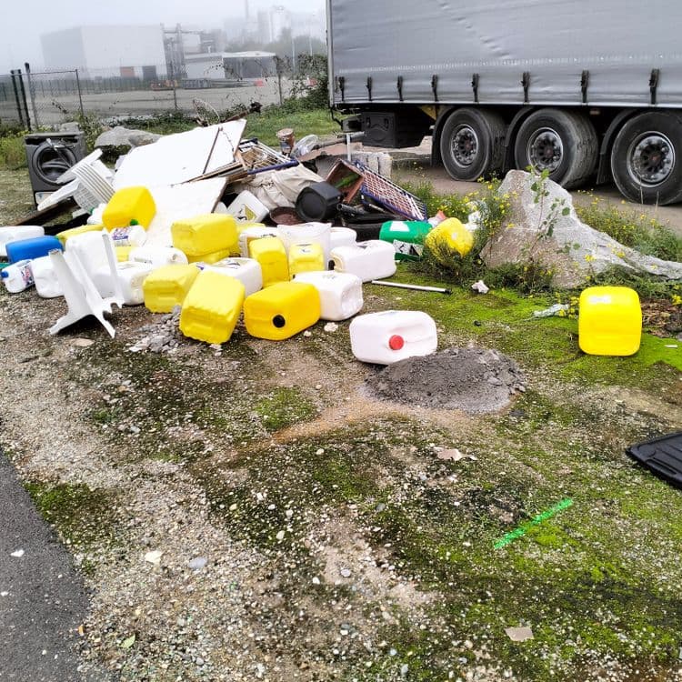 Machine à laver, bidons de javel vides en grande quantité et déchets divers abandonnés sur un parking poids lourds 