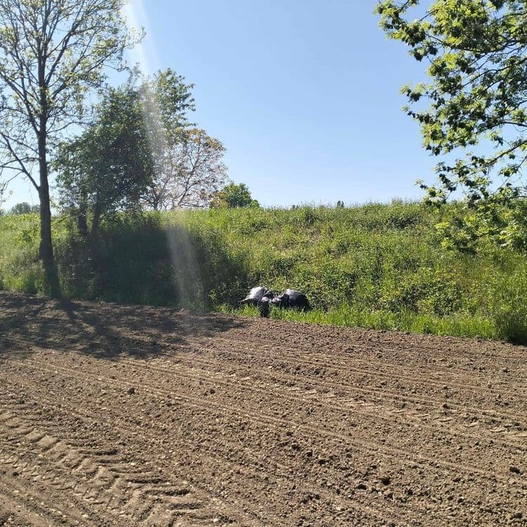 Trois gros sacs poubelles abandonnés au bord d'un champ en contrebas d'une route 