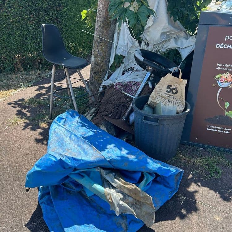 Les déchets abandonnés comprennent :

*   **Mobilier et gros objets encombrants** :
    *   Une chaise de bar noire, estimée à 4 kilogrammes.
    *   Un tabouret de bureau (base sans dossier), estimé à 6 kilogrammes.
    *   Une tablette ou planche avec ses pieds métalliques, estimée à 7 kilogrammes.

*   **Plastiques divers** :
    *   Une bâche bleue de grande taille, estimée à 3 kilogrammes.
    *   Plusieurs morceaux de bâches ou tissus blancs, pour un poids total d'environ 4 kilogrammes.
    *   Une poubelle noire en plastique, estimée à 2 kilogrammes.
    *   Une caisse en plastique noire, contenant des objets divers, pour un poids total d'environ 3 kilogrammes (caisse et contenu).
    *   Une caisse en plastique verte, estimée à 1,5 kilogramme.
    *   Un seau ou une bassine verte, estimé à 0,7 kilogramme.

*   **Métaux et ferraille** :
    *   Une grille métallique ou un ventilateur cassé, estimé à 3 kilogrammes.
    *   Plusieurs pièces métalliques non identifiées (ferraille diverse, partie de vélo), pour un poids total d'environ 7 kilogrammes.

*   **Autres déchets** :
    *   Un sac en papier contenant des petits déchets, estimé à 1 kilogramme.
    *   Un pot de fleur en terre cuite, estimé à 1,5 kilogramme.
    *   Des déchets mélangés non identifiés (petits débris, terre), pour un poids total d'environ 8 kilogrammes.