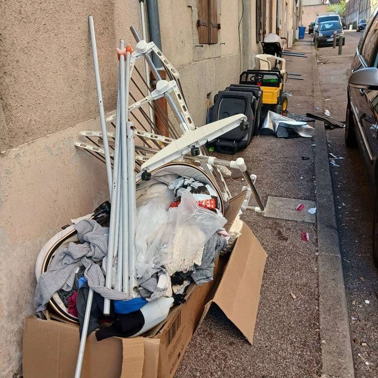 Voici le relevé des déchets abandonnés :

*   **Étendages à linge** : 2 unités (un grand modèle, un plus petit ou partiel). Poids estimé : 6 kg.
*   **Cartons d'emballage** : 1 grande boîte en carton. Poids estimé : 0,8 kg.
*   **Vêtements et textiles** : L'équivalent d'environ 1 grand sac poubelle rempli. Poids estimé : 7 kg.
*   **Sacs plastiques** : Environ 3 à 4 sacs, certains contenant des textiles. Poids estimé : 0,1 kg.
*   **Sièges auto ou éléments de poussette** : 3 unités. Poids estimé : 21 kg.
*   **Jouet d'enfant** (type tracteur) : 1 unité. Poids estimé : 4 kg.
*   **Déchets métalliques et plastiques divers** : Plusieurs pièces (tôles froissées, éléments non identifiés). Poids estimé : 3 kg.
*   **Déchets épars** (papiers, emballages) : Quelques petits éléments dispersés sur le trottoir. Poids estimé : Moins de 0,1 kg.