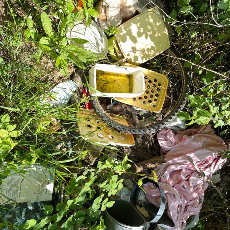 Voici une estimation des déchets présents sur l'image :

*   **Plastique divers** : Bacs, fragments de récipients, couvercles. Estimation : 2 kg, environ 5 à 7 éléments distincts.
*   **Textile** : Vêtements, probablement en coton ou matière synthétique. Estimation : 0.5 kg, un amas de tissu.
*   **Métal** : Roue de vélo (partie en métal), débris métalliques non identifiés. Estimation : 1 kg, une roue et quelques petits fragments.
*   **Papier/Carton** : Documents imprimés, potentiellement emballages. Estimation : 0.2 kg, quelques feuilles éparses.
*   **Divers** : Seau en plastique ou autre matériau. Estimation : 0.3 kg, un seau.


